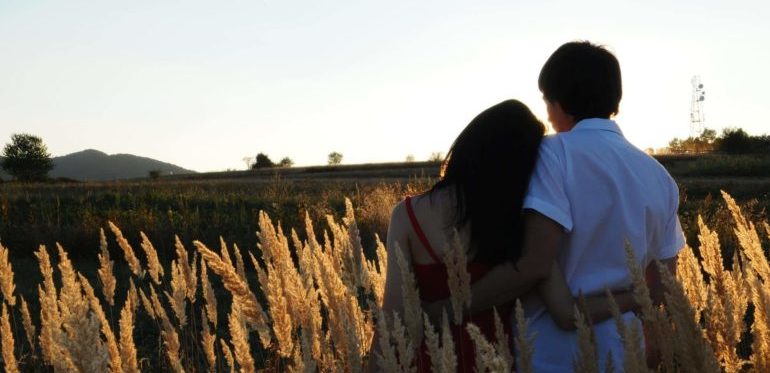 A couple hugging on an open field.