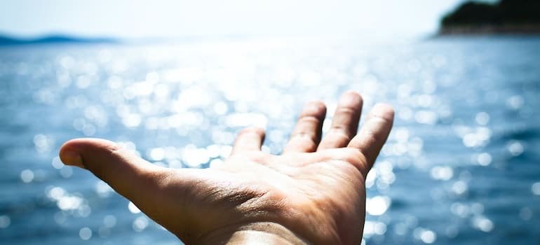 A person’s hand extended toward a body of water.