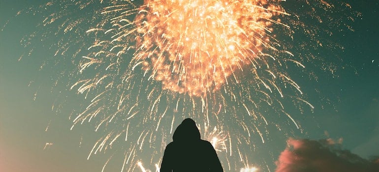 A hooded individual watching a fireworks display in the sky outdoors.