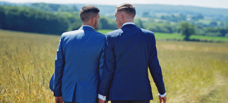 A couple of men in suits walking in a field while holding hands.