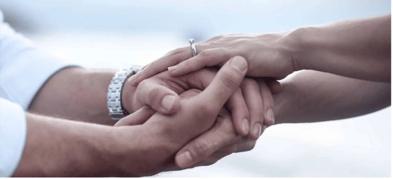 A close-up of two people holding hands in support.