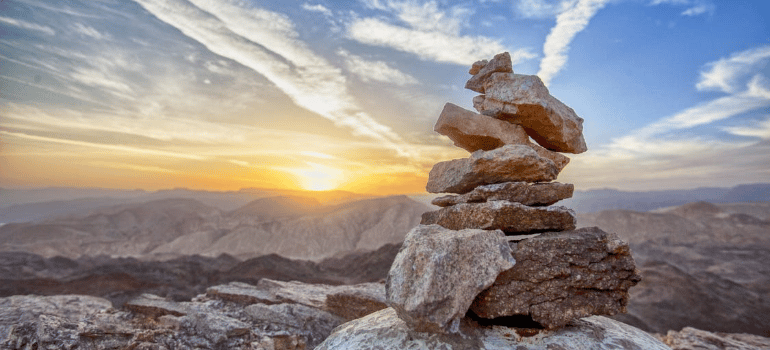 A photo of piled brown stones on a mountaintop behind a rising sun.