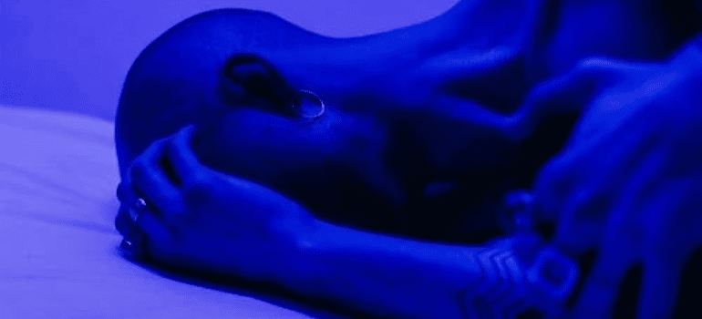 A person lying in bed under blue lighting.