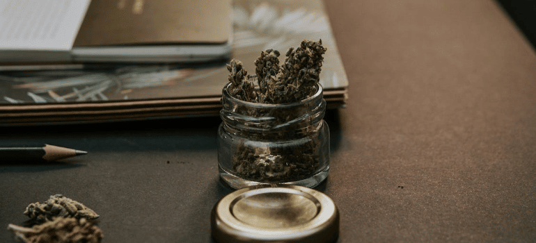 A close-up of marijuana in a glass container on a desk.