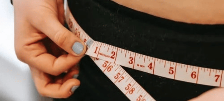 A close-up of a woman measuring her waist.