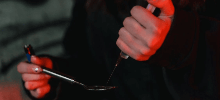 A close-up of a person collecting an illicit substance from a spoon into a syringe.