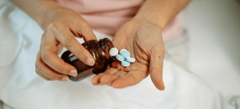 A close-up of a person taking pills out of a bottle onto their hand.