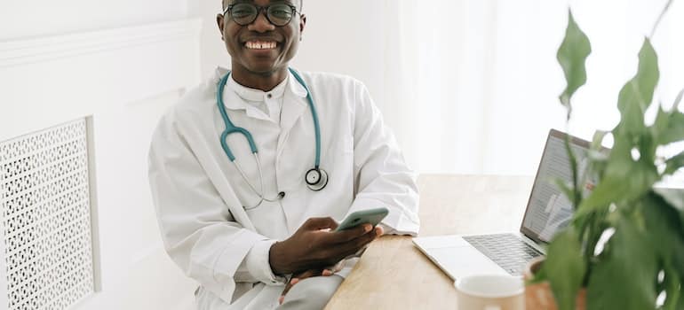 A smiling doctor in a lab coat holding a smartphone.