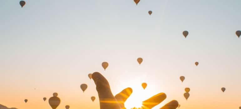 A person’s hand stretched toward hot air balloons in the evening sky.