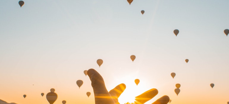 A person holding their hand toward hot air balloons at sunset.