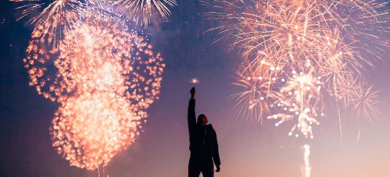 A man with his hand raised under fireworks. 