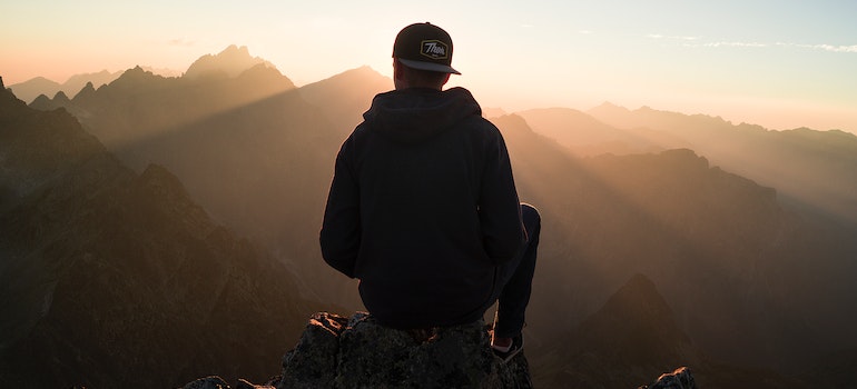 A silhouette of a man sitting on a mountain edge at sunset.