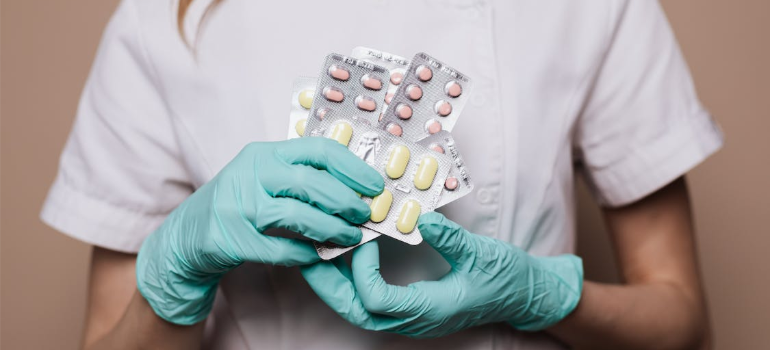 A close-up of a nurse in gloves holding tablets of pills.