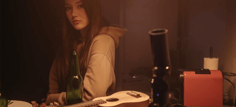 A woman wearing a hoodie looking at a bong indoors.