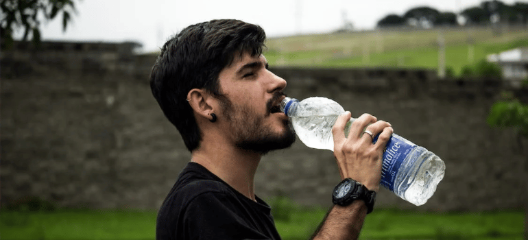 A man in a black shirt drinking water outdoors.
