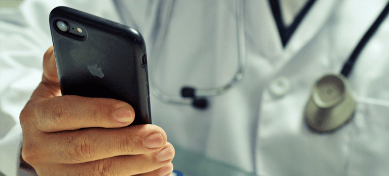 A close-up of a doctor with a stethoscope holding a mobile phone.