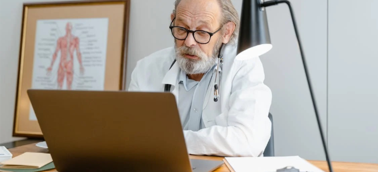 An older doctor working on a laptop in his office.