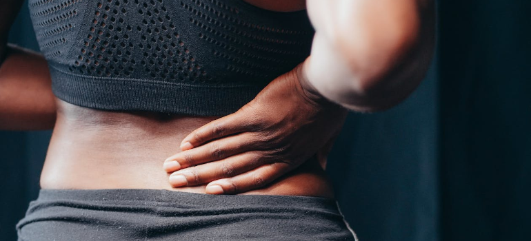A close-up of a woman holding her lower back in pain.