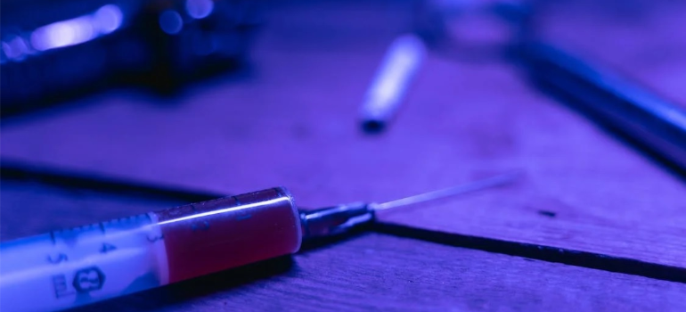 A syringe on a brown table under purple lighting.