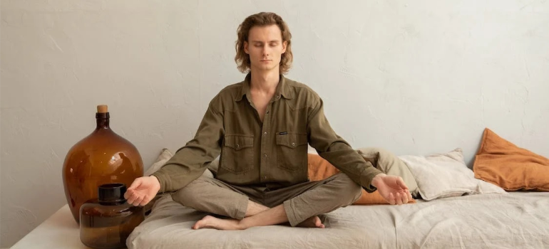 A man meditating in a lotus pose on a sofa.