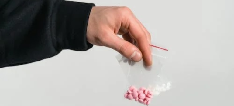 A close-up of a person’s hand holding bags of white and pink pills.