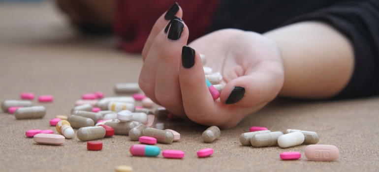 A close-up of a person’s hand on the floor, holding medicine pills.