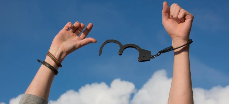 A crop of a person’s hand removing handcuffs against a clear sky.