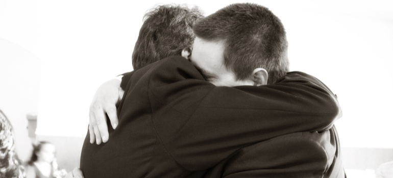 A black-and-white close-up of a father and son hugging outdoors.