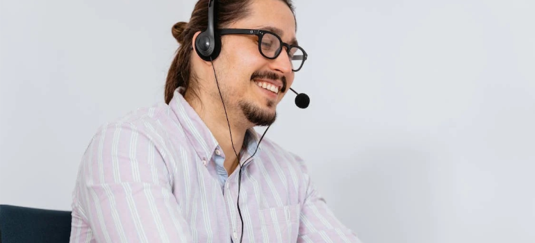 A close-up of a smiling man in a long-sleeved shirt speaking into a headset.