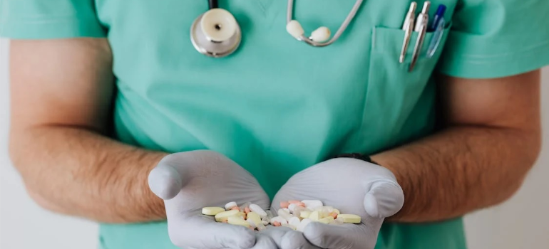 A doctor in a scrub suit holding pills in his hands.