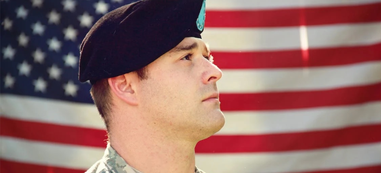 A man in an army uniform in front of a US flag.