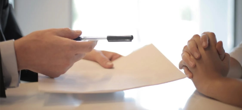 A close-up of a person handing another a pen to sign a contract. 
