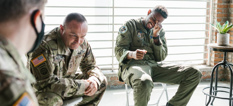 Men in army uniforms bantering during a group therapy session indoors.