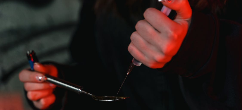 A person using a spoon and a syringe to prepare an illicit substance.