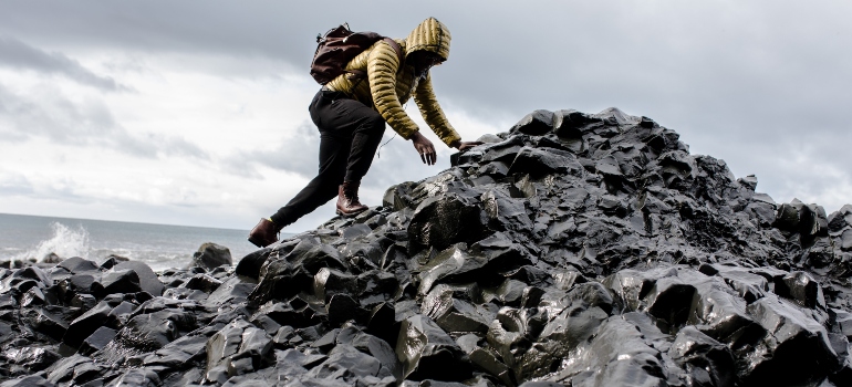 person climbing on a pile of rocks with the sea in the background