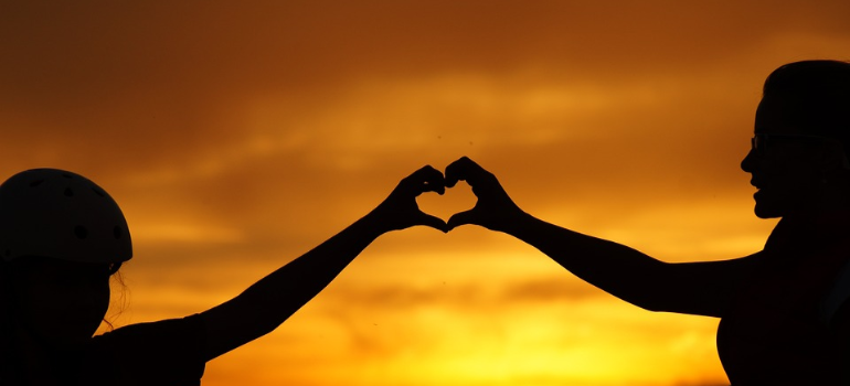 Two silhouettes of people forming a heart sign with their joined hands, representing self-efficacy in addiction recovery.