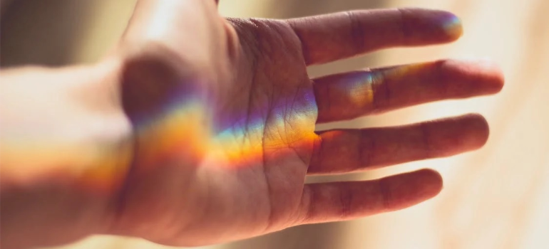 A close-up of a person’s open hand, with rainbow colors reflecting on it.