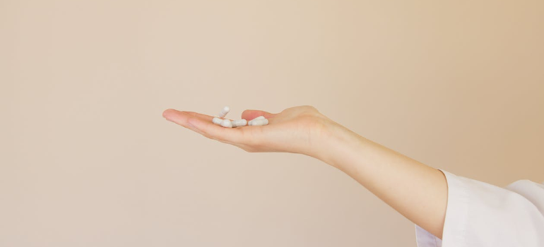A doctor’s extended hand offering medication pills.
