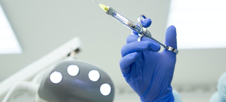a hand in a purple latex glove holding a syringe as a part of anesthesia