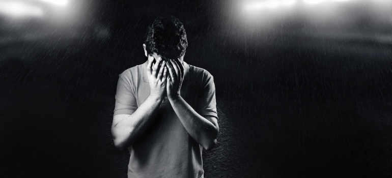 black and white photo of a man standing outside holding his face in his hands, representing burnout as an underlying cause of addiction