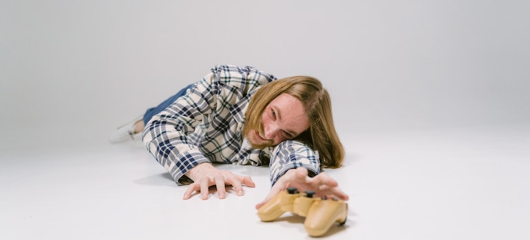 Man crawling on the floor trying to reach a game console showing the difference between physical and psychological addiction.