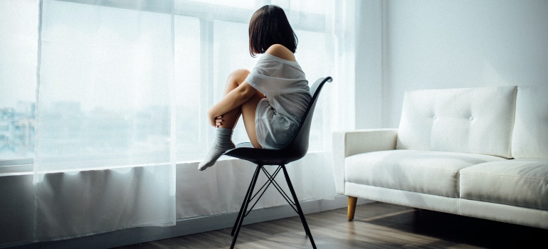 Depressed woman sitting on a chair and looking through the window