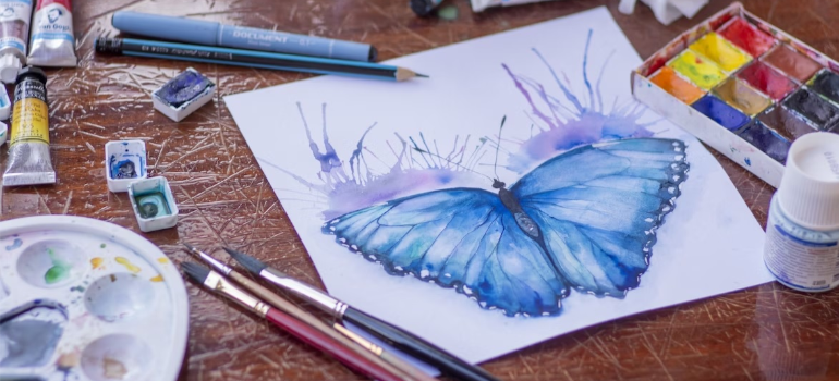 A close-up of a painting of a blue butterfly on a table next to art supplies, illustrating a holistic approach to recovery employing alternative therapies for addiction.