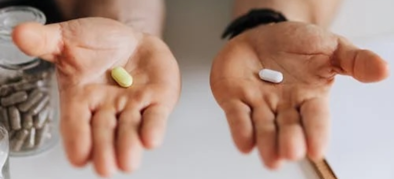 A close-up of a medical professional presenting a pill in each hand.