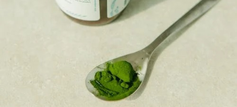A spoon with a green dietary supplement on a table, symbolizing the importance of nutrition in alcohol addiction treatment.