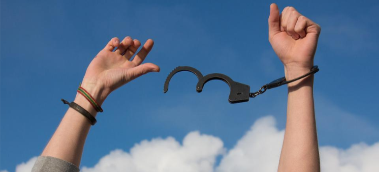 A close-up of a person’s hands removing handcuffs under a blue sky.