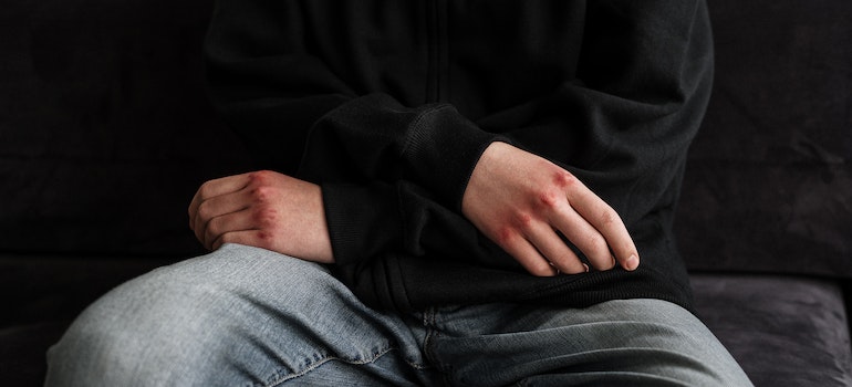 injured hands crossed over a man's lap representing how trauma shapes addiction and healing