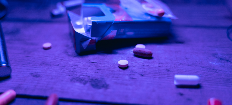 On a table there is a variety of pills of different shapes and sizes, and a pack of cigarettes.