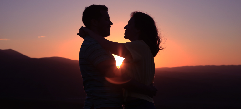 Two people, man and woman, hugging each other as the sun goes down.
