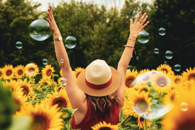 A woman among sunflowers with her hands in the air and a hat on her head